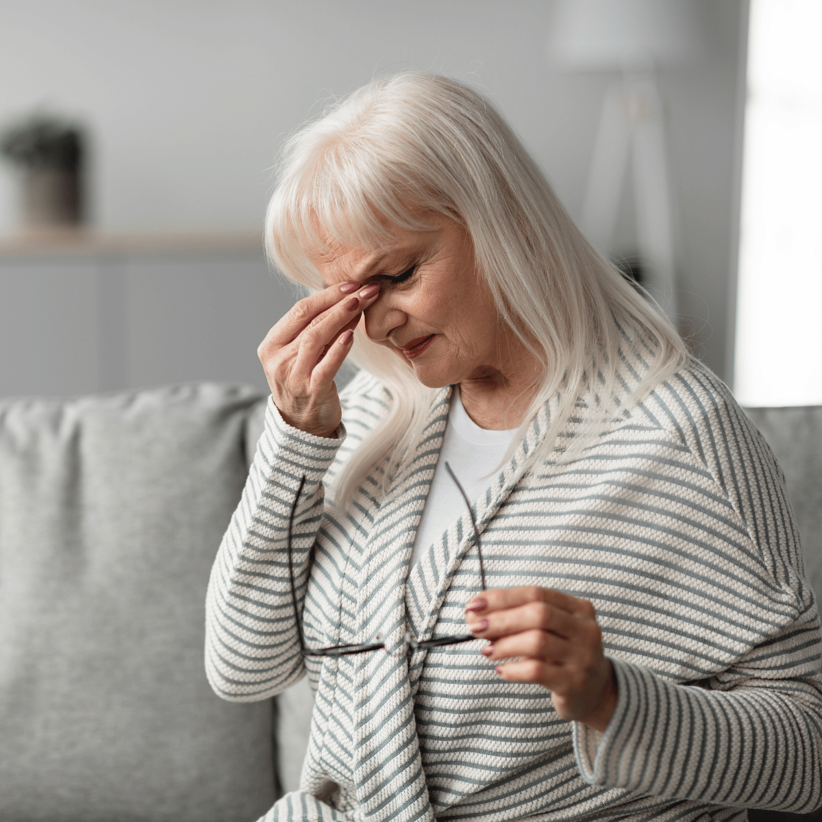 Juckendes Auge bei älterer Frau Ältere Frau reibt sich wegen eines juckenden und gereizten Auges das Auge und hält ihre Lesebrille in der Hand.